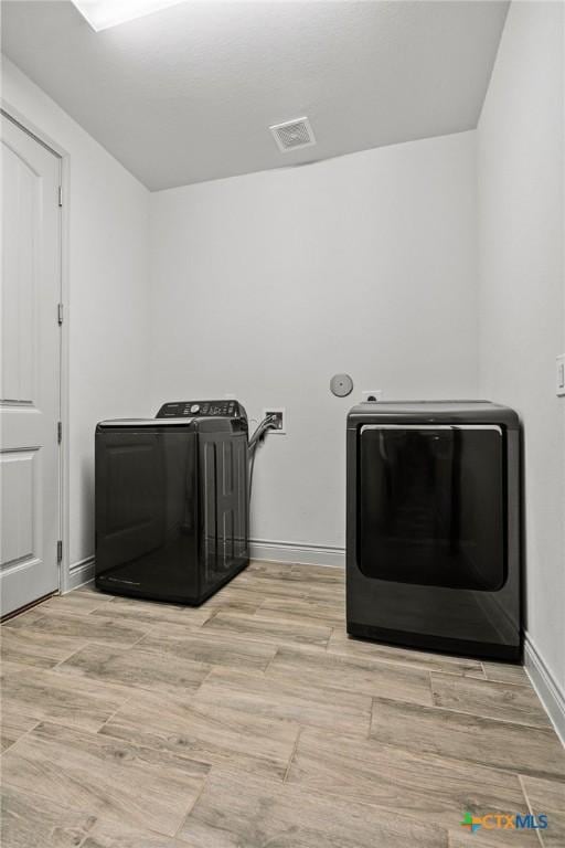 clothes washing area featuring washer and clothes dryer and light wood-type flooring