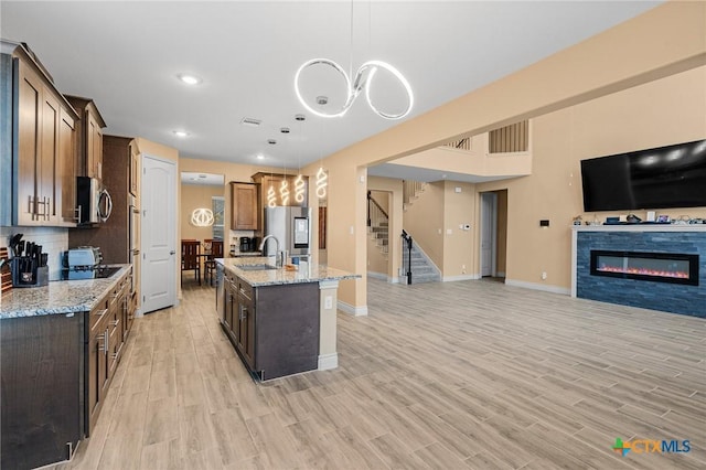 kitchen featuring light hardwood / wood-style flooring, an island with sink, stainless steel appliances, and decorative light fixtures