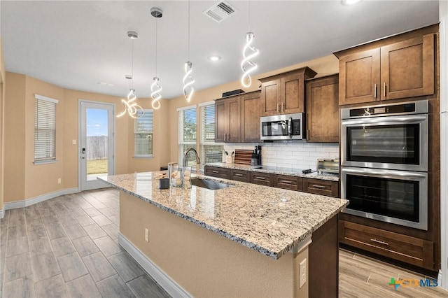 kitchen with pendant lighting, sink, an island with sink, and appliances with stainless steel finishes