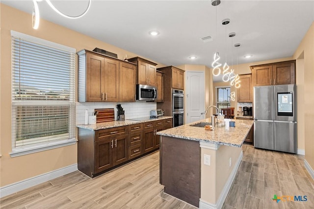 kitchen featuring sink, an island with sink, decorative light fixtures, appliances with stainless steel finishes, and light wood-type flooring