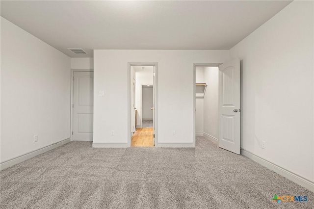 unfurnished bedroom with a spacious closet, a closet, and light carpet