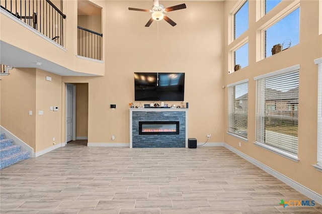 unfurnished living room featuring ceiling fan, a towering ceiling, and light wood-type flooring