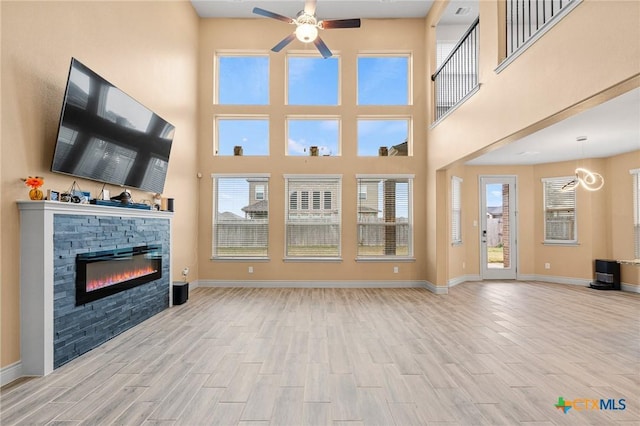 unfurnished living room with a stone fireplace, ceiling fan, a towering ceiling, and light wood-type flooring