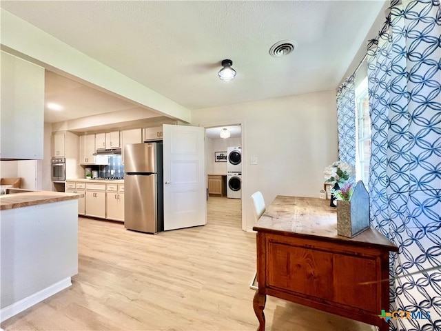 kitchen with visible vents, stacked washing maching and dryer, stainless steel appliances, under cabinet range hood, and light wood-type flooring