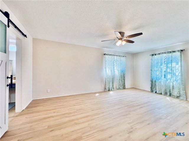 unfurnished room featuring light wood finished floors, a textured ceiling, a ceiling fan, and a barn door