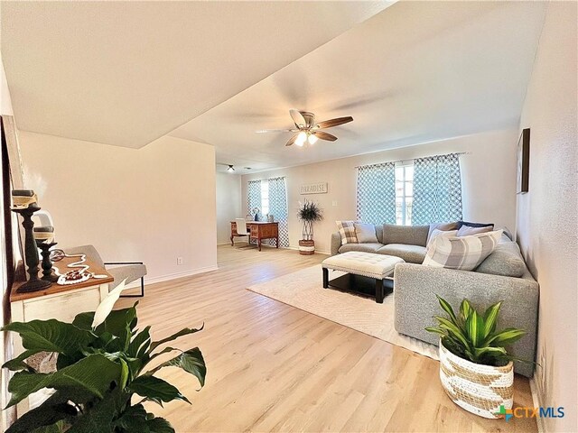 living area featuring baseboards, ceiling fan, and light wood finished floors