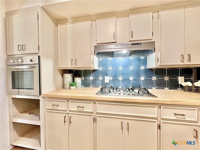 kitchen with under cabinet range hood, wood counters, backsplash, stainless steel appliances, and white cabinets