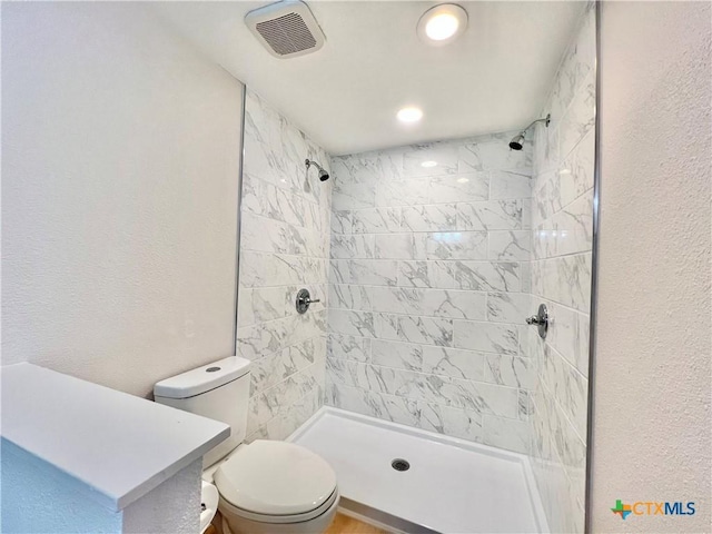 full bath featuring a shower stall, toilet, a textured wall, and visible vents