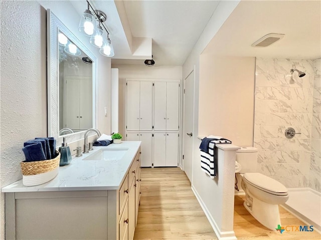 bathroom with visible vents, toilet, a tile shower, wood finished floors, and vanity