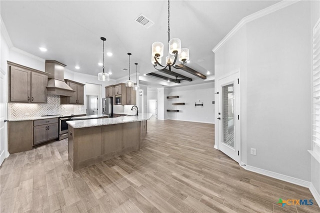 kitchen with custom range hood, stainless steel appliances, sink, hanging light fixtures, and an island with sink