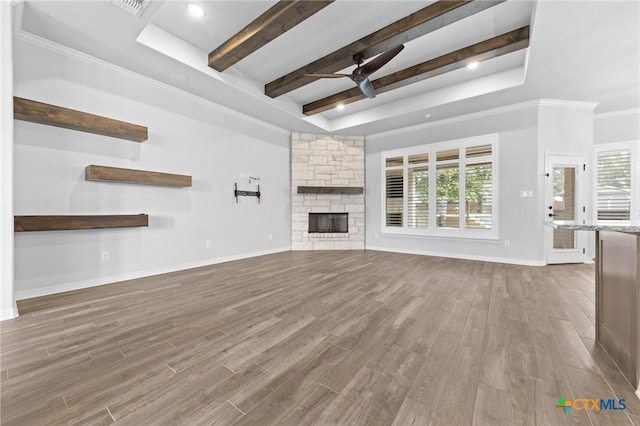 unfurnished living room with a stone fireplace, crown molding, ceiling fan, a tray ceiling, and wood-type flooring