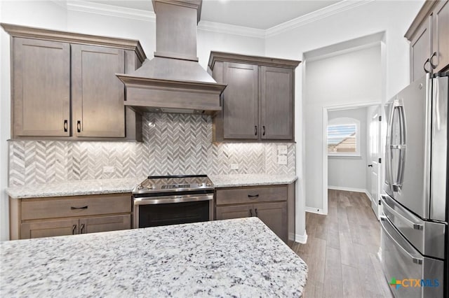 kitchen featuring backsplash, light stone countertops, custom range hood, and stainless steel appliances