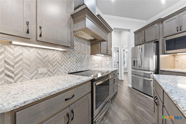 kitchen with stainless steel appliances, light stone counters, crown molding, hardwood / wood-style floors, and custom exhaust hood