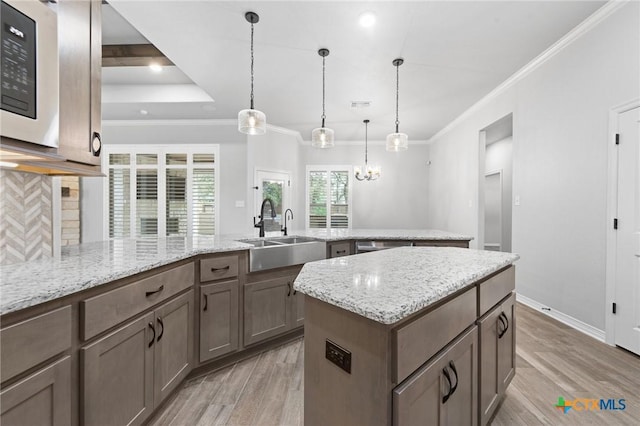 kitchen featuring light stone countertops, sink, light hardwood / wood-style floors, decorative light fixtures, and a kitchen island