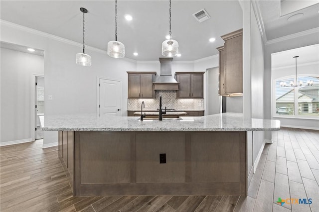 kitchen with hanging light fixtures, ornamental molding, light stone countertops, tasteful backsplash, and custom range hood