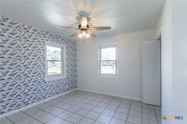 spare room featuring ceiling fan, wallpapered walls, light tile patterned floors, and baseboards