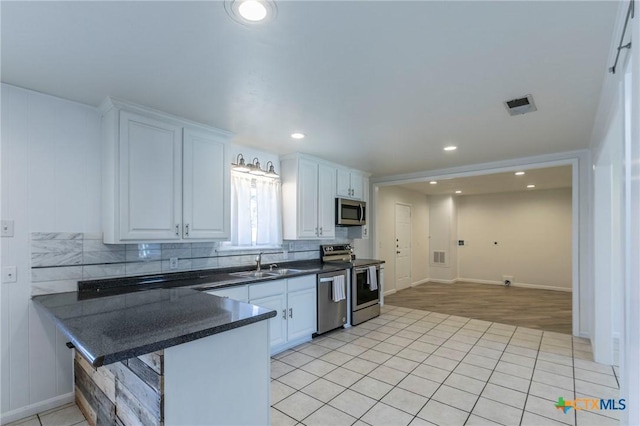 kitchen featuring stainless steel appliances, a peninsula, a sink, white cabinetry, and tasteful backsplash