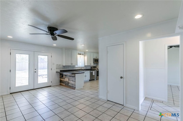 kitchen with french doors, light tile patterned floors, dark countertops, appliances with stainless steel finishes, and a peninsula