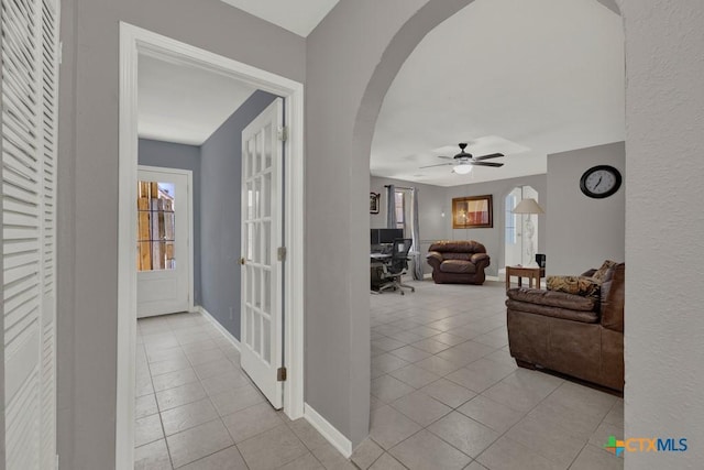 corridor with light tile patterned floors, baseboards, and arched walkways