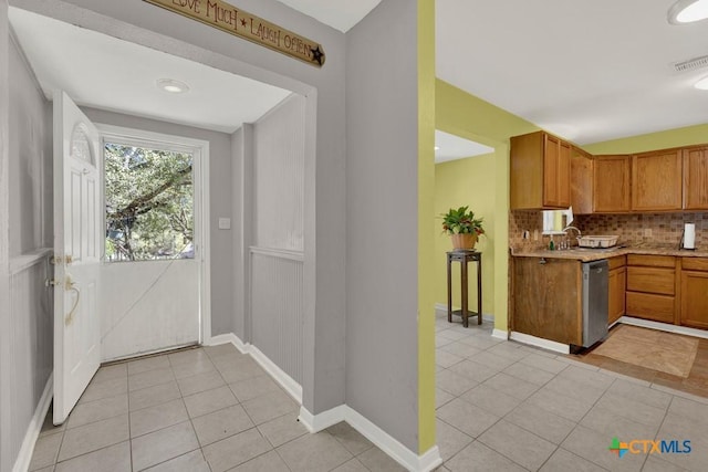 kitchen featuring light tile patterned floors, light countertops, backsplash, brown cabinetry, and dishwasher