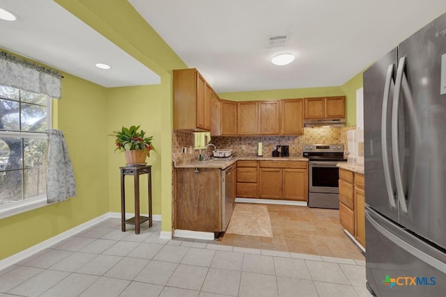 kitchen featuring under cabinet range hood, stainless steel appliances, visible vents, light countertops, and tasteful backsplash