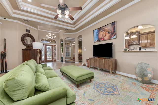 living room with a tray ceiling, french doors, ornamental molding, and ceiling fan with notable chandelier