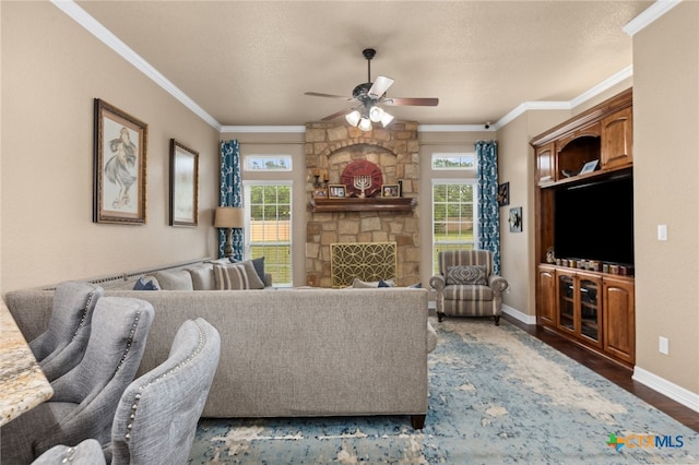 living room featuring ceiling fan, a textured ceiling, a stone fireplace, crown molding, and dark wood-type flooring