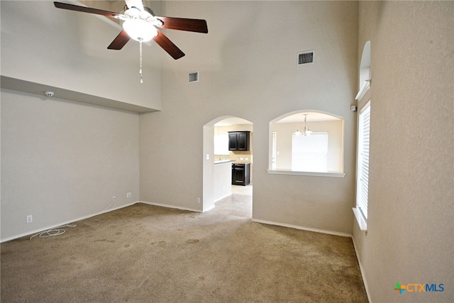 unfurnished living room featuring a high ceiling, carpet, and ceiling fan with notable chandelier