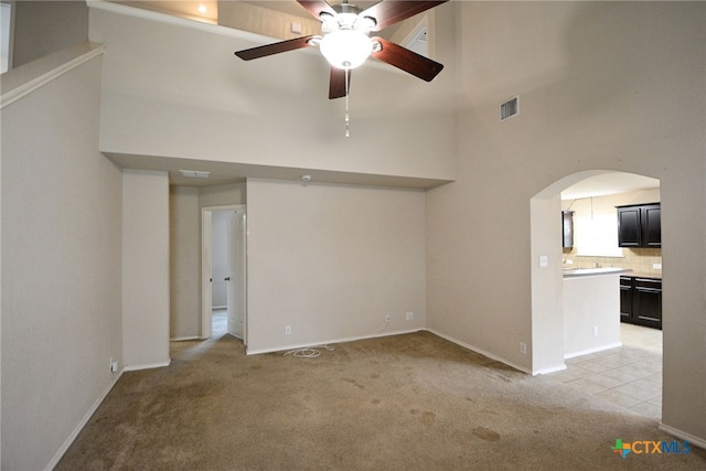 unfurnished living room featuring a high ceiling, light carpet, and ceiling fan