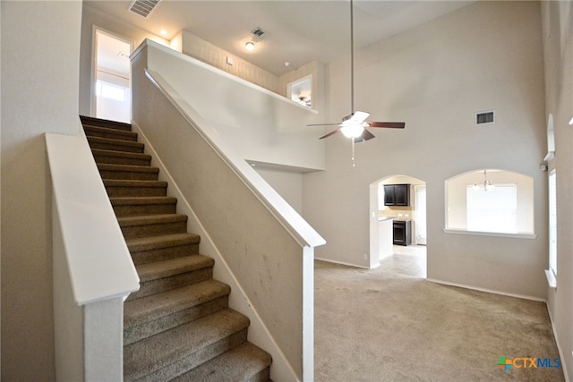 staircase featuring a high ceiling, ceiling fan, and carpet flooring