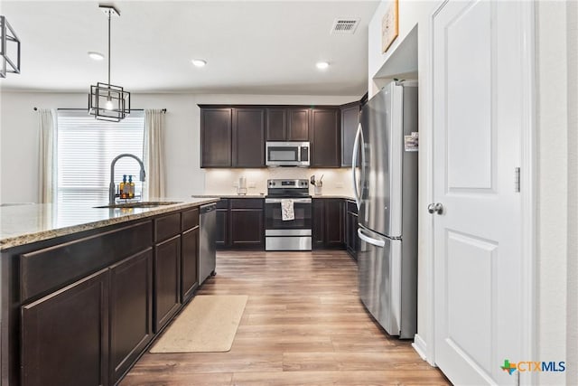 kitchen featuring visible vents, appliances with stainless steel finishes, a sink, dark brown cabinetry, and light stone countertops