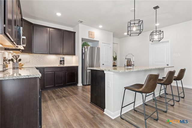 kitchen featuring dark wood-type flooring, visible vents, dark brown cabinets, freestanding refrigerator, and decorative backsplash