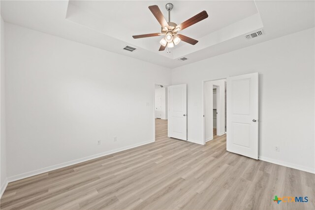 unfurnished bedroom with light hardwood / wood-style floors, ceiling fan, and a raised ceiling