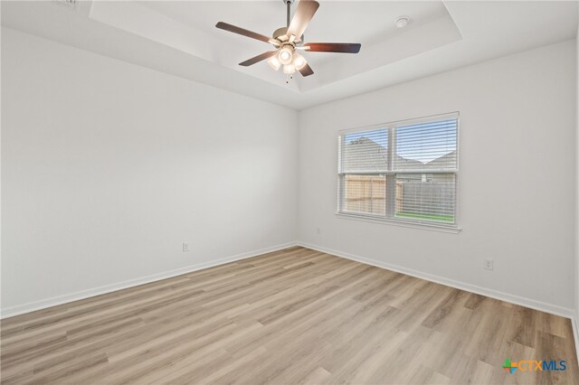 empty room featuring light hardwood / wood-style floors, ceiling fan, and a raised ceiling