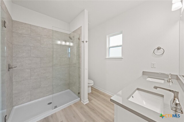 bathroom featuring a tile shower, wood-type flooring, toilet, and vanity