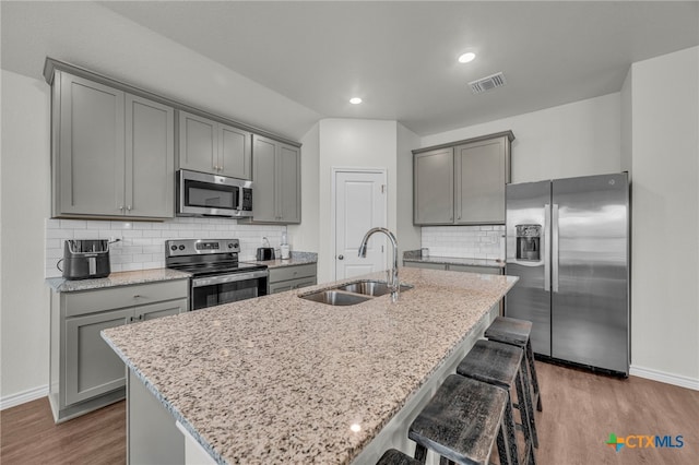 kitchen featuring dark wood-type flooring, sink, light stone counters, an island with sink, and stainless steel appliances