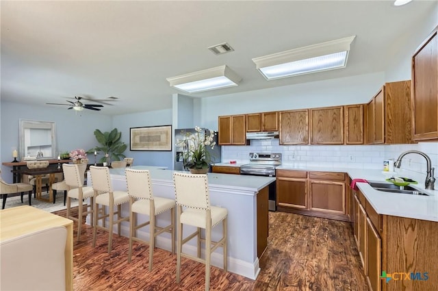kitchen featuring brown cabinetry, visible vents, under cabinet range hood, a sink, and stainless steel appliances