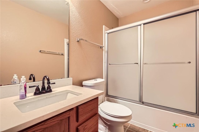 bathroom featuring vanity, tile patterned floors, bath / shower combo with glass door, toilet, and a textured wall