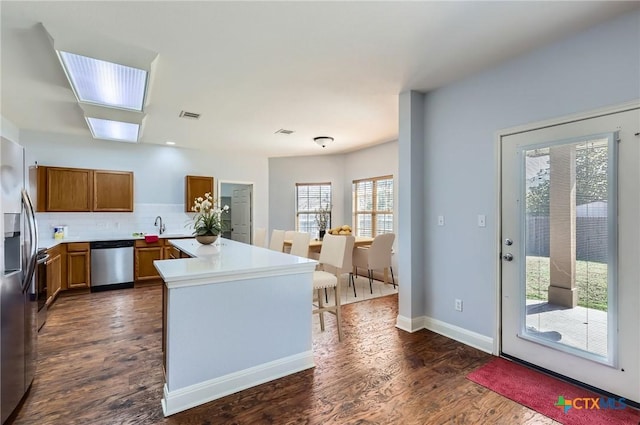 kitchen with backsplash, visible vents, brown cabinets, stainless steel appliances, and dark wood-type flooring