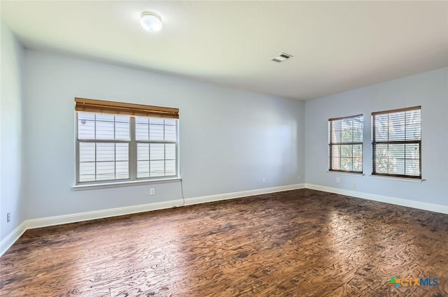 spare room featuring baseboards, dark wood-style flooring, and visible vents