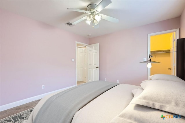 carpeted bedroom with visible vents, a closet, baseboards, a walk in closet, and a ceiling fan