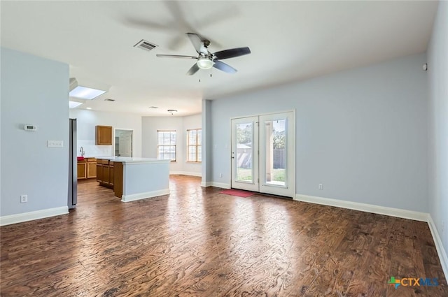 unfurnished living room with ceiling fan, visible vents, baseboards, and dark wood finished floors
