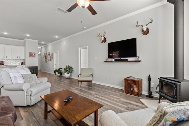 living area featuring visible vents, a ceiling fan, wood finished floors, baseboards, and a wood stove