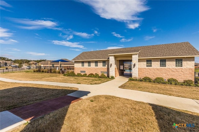 exterior space featuring stone siding, a shingled roof, a front lawn, and fence