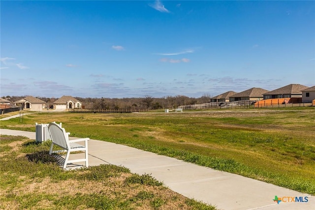 view of community featuring fence, a lawn, and a residential view