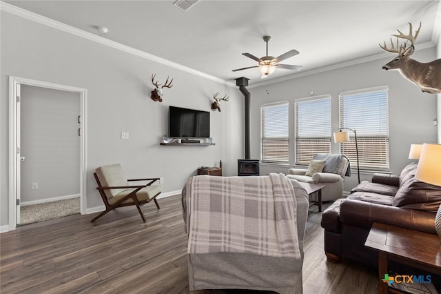 living area featuring a ceiling fan, dark wood-style floors, crown molding, baseboards, and a wood stove