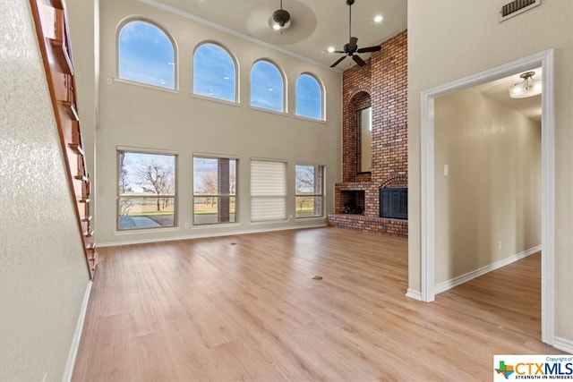 unfurnished living room with a fireplace, a towering ceiling, plenty of natural light, and light hardwood / wood-style flooring