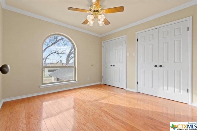 unfurnished bedroom with ceiling fan, two closets, light hardwood / wood-style floors, and crown molding