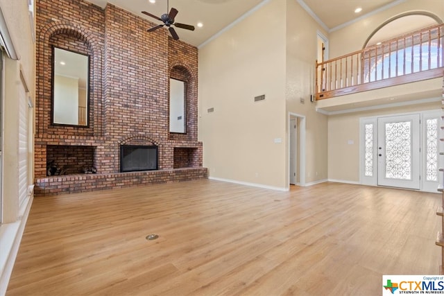 unfurnished living room featuring a high ceiling, light wood-type flooring, crown molding, and a brick fireplace