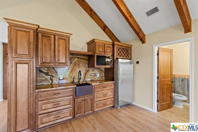 kitchen with lofted ceiling with beams, backsplash, appliances with stainless steel finishes, sink, and light hardwood / wood-style floors